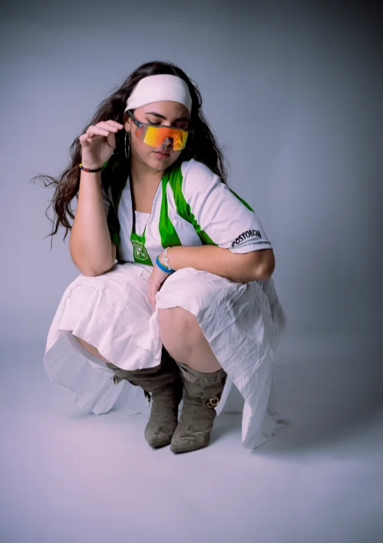 Artista agachada con vincha y anteojos naranjas