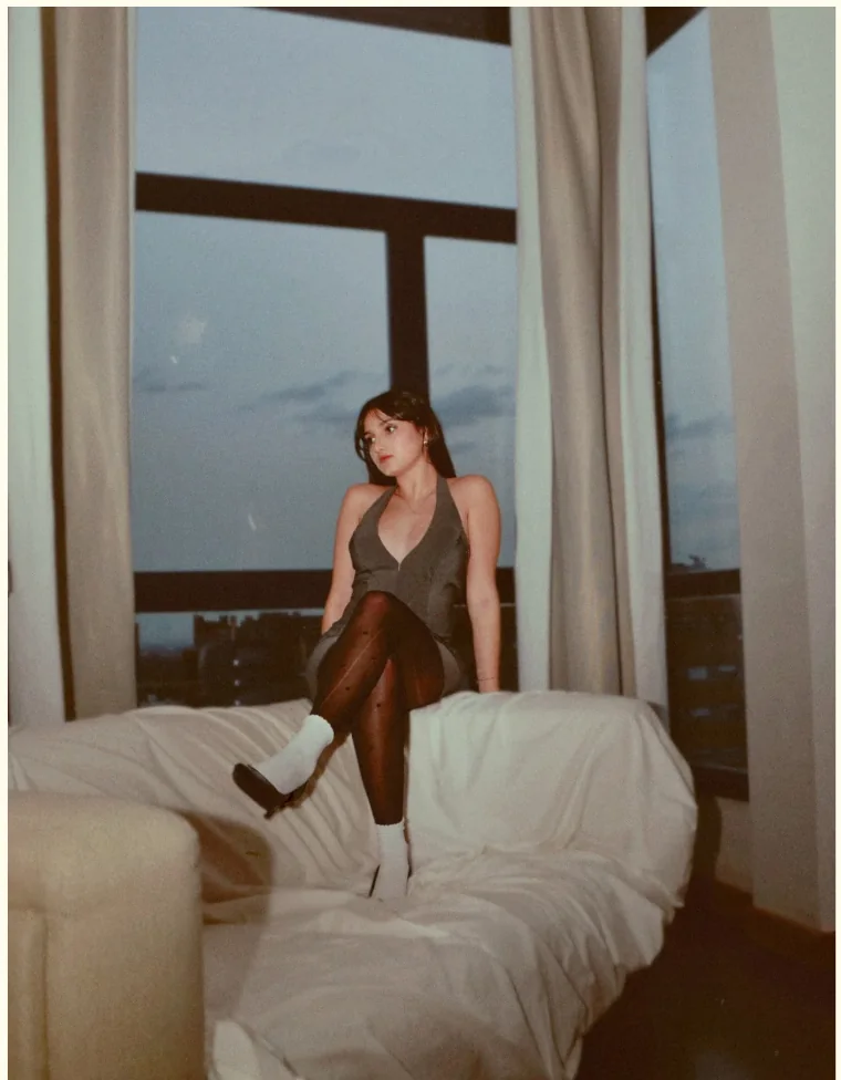 Retrato sentada sobre una cama blanca junto a la ventana